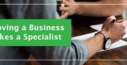 2 people meeting at a table. there are papers on the table and one man is taking notes. A green block with white text displays "Moving a Business Takes a Specialist"